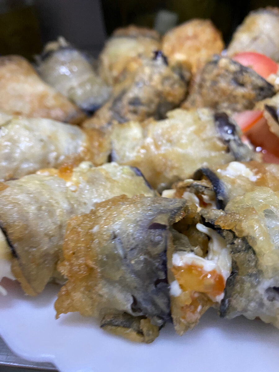 Баклажан нарезать длинными слайсами,обвалять в муке и яйце,обжарить на растительном масле до золотистой корочки. Помидор нарезать полукружочками.Майонез,чеснок ,сыр,специи смешать . Выложить на обжаренный баклажан наш соус и помидор,свернуть рулетиком. Если не держится ,можно скрепить шпажками для канапе . Приятного аппетита!