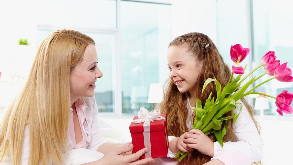    Мама поздравляет дочку с днем рождения. Она улыбается, дарит цветы и протягивает дочке красную подарочную коробку:Freepik