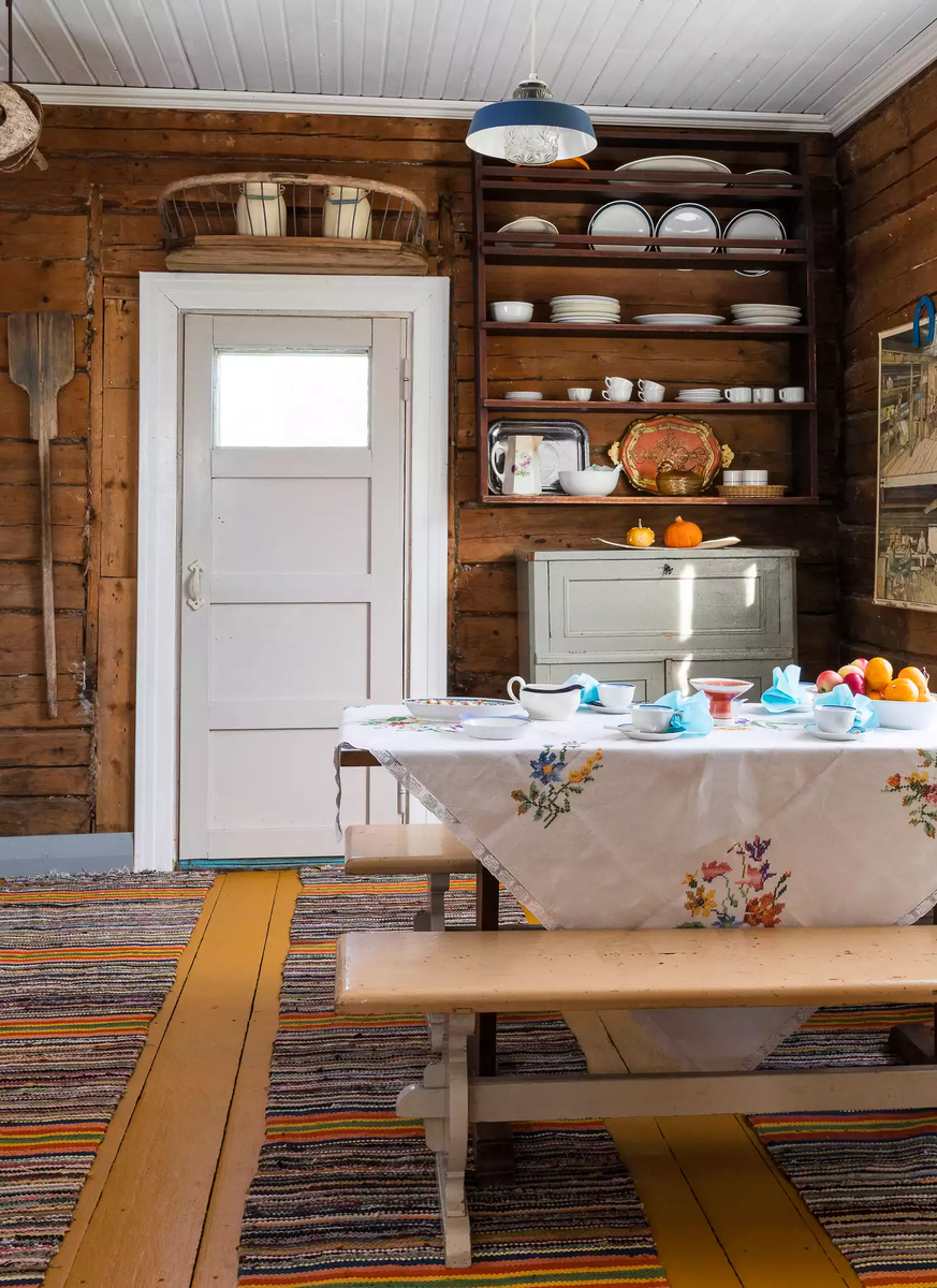 Внутри — классическая финская дача середины прошлого века. Деревянные полы, входная дверь с окошком, скатерть с вышивкой, скамья вместо стульев, открытые полки с повседневной посудой и даже лопата на стене у входа
