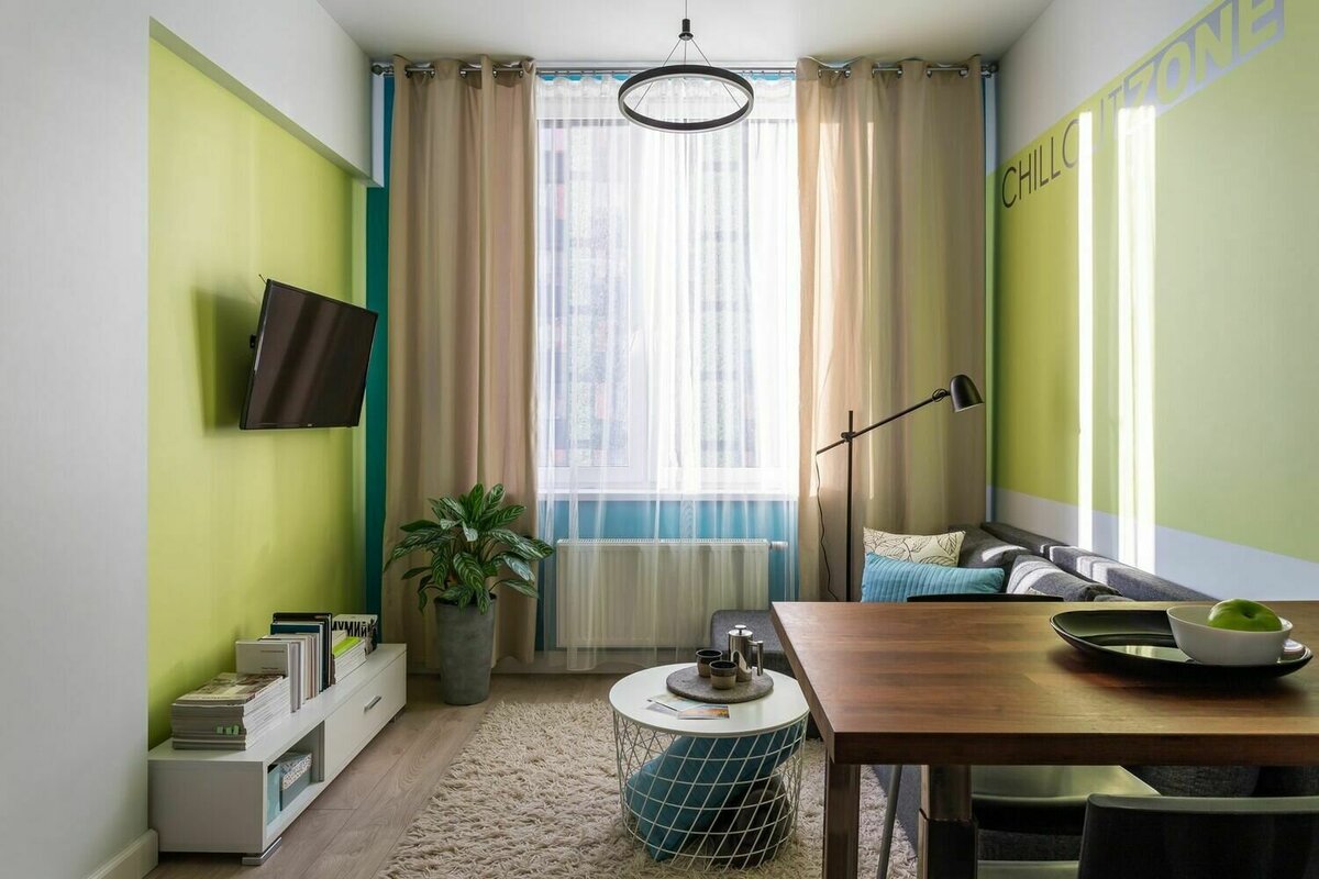 Мебель подбирали лаконичных форм и нейтральных тонов, чтобы уравновесить буйство красок в отделке. Под телевизором разместили невысокую тумбу белого цвета. Листайте галерею