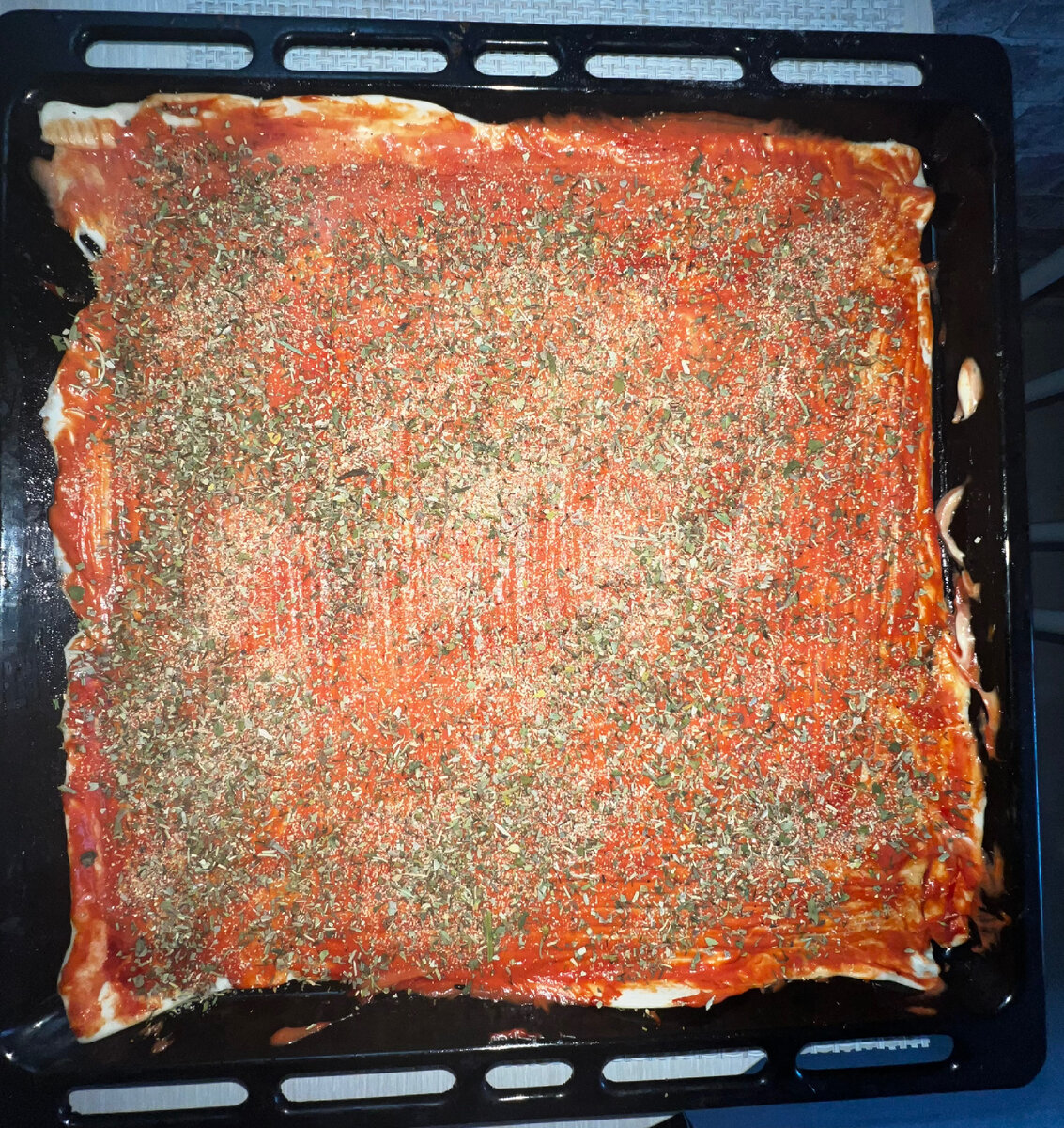 Раскатать тесто по листу. Тесто смажьте сначала томатным соусом, потом майонезом. Вилкой сделайте проколы в нескольких местах, чтобы пицца не вздулась во время пропекания. Посыпьте итальянскими травами.