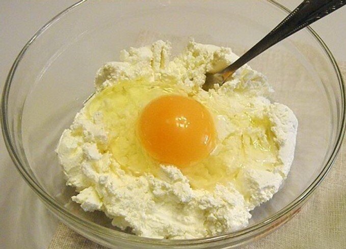 Процесс приготовления: 
1. В посуду для замеса теста положите творог. Вбейте к нему куриное яйцо и добавьте сахар и немного ванилина.

2. С помощью вилки хорошо перемешайте эти ингредиенты.
Ингредиенты: 
Творог – 200 г.
Сахар и манная крупа – по 3 ст. л.
Сметана – 5 ст. л.
Яйцо – 1 шт.
Сливочное масло – 2 ст. л.
Разрыхлитель для теста – 1 ч. л.

