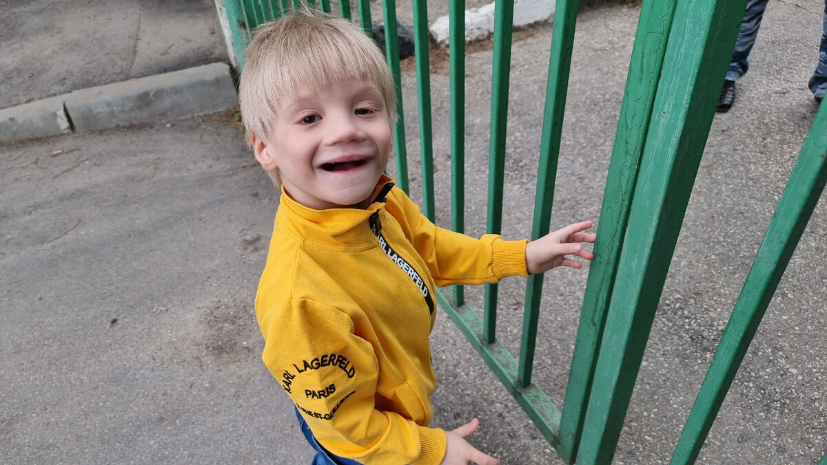 На фото мой маленький герой уверенно стоит возле тех самых ворот, у которых я его когда-то увидела впервые. Он стоял на слабеньких дрожащих согнутых в коленках ножках, синюшно-бледный, с длинными, развивающимися белокурыми волосами. Сегодня он жив, счастлив, любим, растёт и развивается не только его тело, но и интеллект.