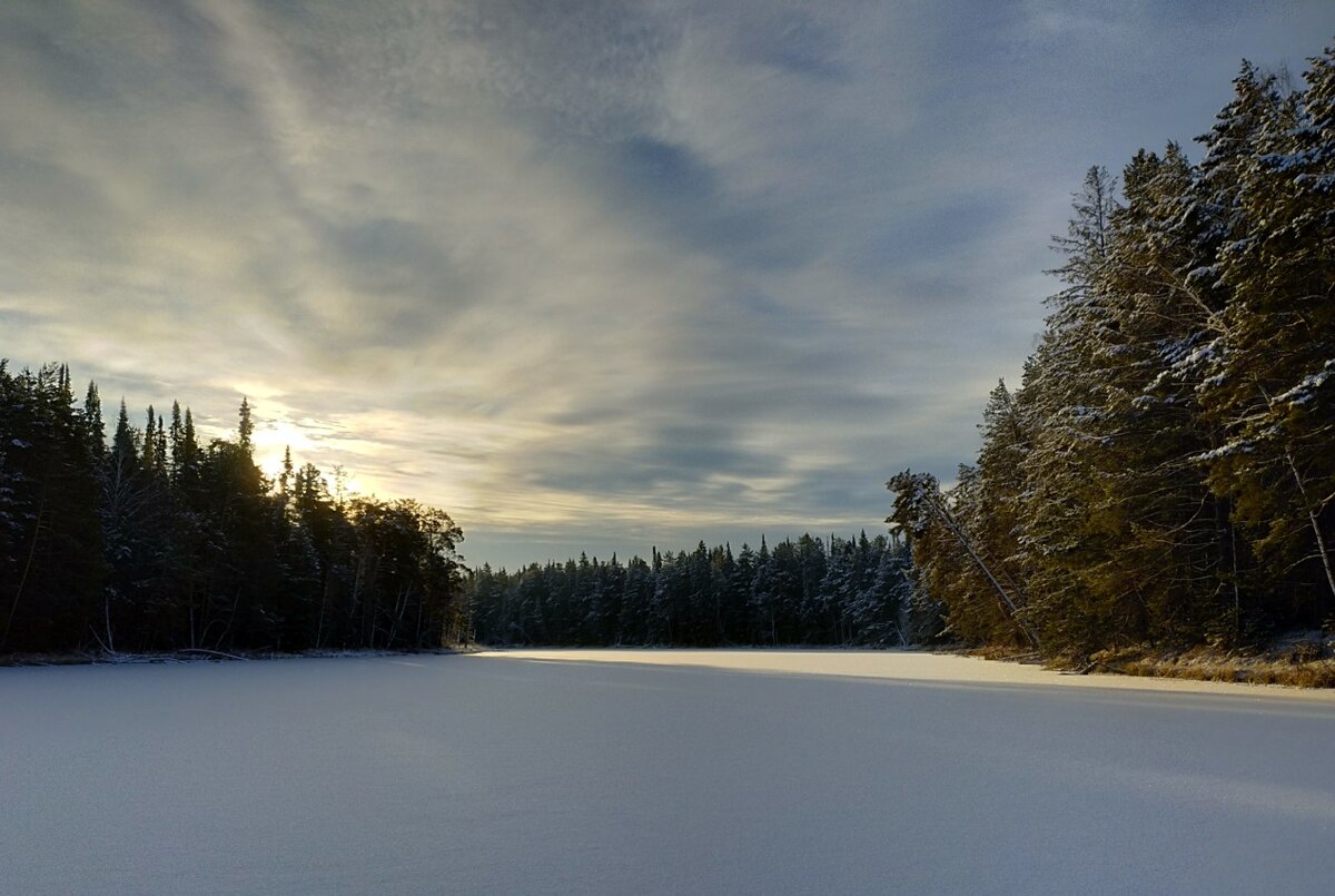 День длинных теней. Декабрь. День короткий, а тени длинные, так как солнышко невысоко поднимается над горизонтом.Чистейший, без самых малых следочков снег, расстилается огромным покрывалом впереди. Молчаливая тайга величаво наблюдает за фотографом со всех сторон. А за изгибом озера солнышко щёдро дарит свет всей природе.