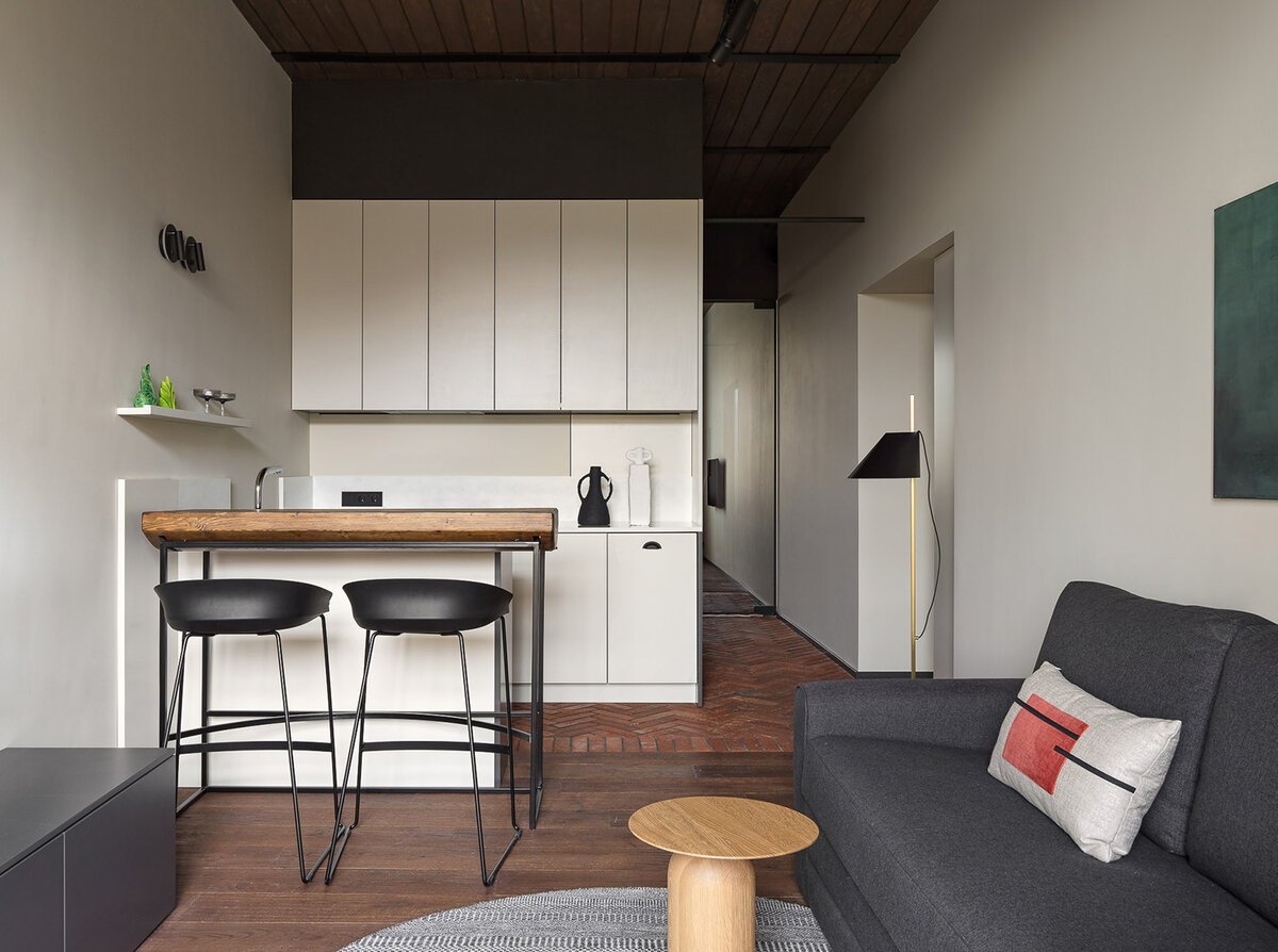 Кухня объединена с гостиной. Из необычного: темные деревянные панели на потолке и разное напольное покрытие. С помощью первого решения квартире добавили глубины (удивительно, но темный потолок не давит, напротив, делает комнату более объемной). С помощью второго решения отделили зоны кухни и гостиной 