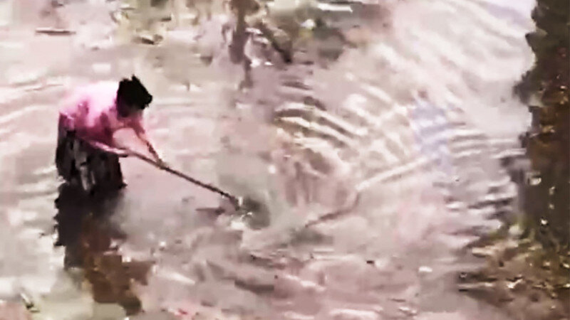     Женщина со шваброй очищает ливневку от грязи. "МК", кадр из видео