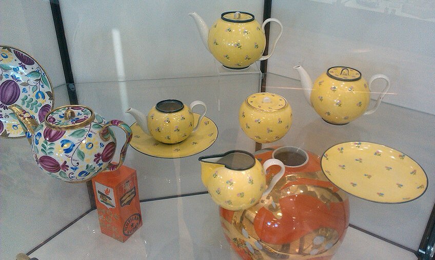 На переднем плане расположены предметы сервиза "Раскидные цветы в жёлтом крытье",  созданном на форме С-1. Это как раз вариант "ситцевой" росписи, копирующей рисунок на ткани.  1937. Слева видим чайник и блюдо на форме С-1, расписанные по эскизу П. Леонова.  Фото взято из свободного доступа в интернете. Листайте галерею вправо.