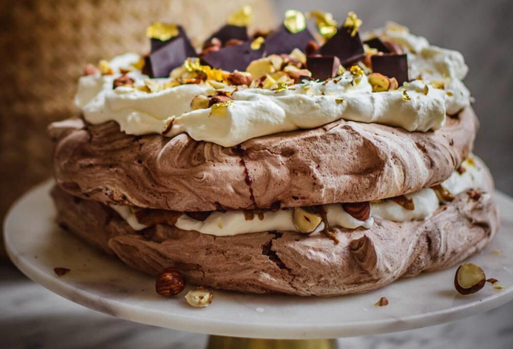 Ингредиенты: Вам нужно 230 г яичных белков
230 г манной сахара
120 г сахарной муки
щепотка соли
15 г кукурузного крахмала
2 столовые ложки голландского какао
800 мл 30-40% взбитых сливок
1 чайная ложка натурального ванильного экстракта
140 г миндального / арахисового масла
Горсть фундука или других орехов
Шоколад и какао для украшения
Процесс:
Протрите венчик с венчиком каплей уксуса. Нужно обезжирить все на 100%, чтобы смесь хорошо побеждала. Просейте сахарную пудру в миску с крахмалом и отложите.

Положите яичные белки в обезжиренную миску и добавьте щепотку соли. Взбейте их в блендере с помощью баллонного венчика (или ручного миксера) сначала для снижения скорости, а затем постепенно увеличивайте до максимального уровня. Когда яичные белки станут белыми, начните добавлять сахар в ложку, взбивая почти до самого высокого уровня. После того, как весь сахар взбил, смесь следует взбивать в течение еще 7-10 минут, пока белые не станут гладкими, без следов кристаллов сахара. Добавьте ванильный ароматизатор за минуту до окончания взбивания. Затем используйте шпатель, чтобы аккуратно перемешать смесь крахмал / сахарная пудра. Наконец, осторожно перемешайте какао, чтобы оно оставило вас «мраморным» в смеси с яичным белком.

Разогрейте духовку до 120 градусов. Подготовьте бумагу для выпечки на противне и нарисуйте 2 колеса одинакового размера (на расстоянии 5 см друг от друга) диаметром 20 - 23 см. Если колеса не помещаются на одном листе, не стесняйтесь использовать два листа. Разделите снег пополам и выложите ложкой или шпателем на нарисованные колеса, совершенство не приветствуется с этим тортом, напротив, несовершенство является основой успеха. Поставить в духовку и снизить температуру до 90 градусов. Сухой яичный белок в течение 4,5 - 5 часов. Но я должен сказать, что это зависит в первую очередь от вашей духовки. Абсолютно важной информацией при приготовлении этого десерта не является открытие духовки! Если вы откроете его, меренга упадет и станет просто блинчиками. Когда безе кажется сухим (оно должно выглядеть хрустящим на поверхности и мягким внутри - не волнуйтесь, в третий раз вы точно узнаете), выключите духовку и дайте ей поработать. Не открывайте его снова. Через час слегка откройте его и подождите, пока он не станет комнатной температуры. Если трупы правильно запечены, они будут красиво удалены с бумаги для выпечки. Опыт показывает, что лучше сушить Павла больше, чем сушить, поэтому оставьте его там на 5 часов.

А пока готовим взбитые сливки. Я не думаю, что вам нужно подсластить его этим рецептом, но это зависит от вашего вкуса. Поставьте миску и взбейте в холодильник или морозильник на 5-10 минут. Вылейте взбитые сливки в миску со льдом, добавьте ванильную эссенцию и взбейте до густой консистенции. Будьте осторожны, чтобы не взбить взбитые сливки, чтобы избежать масла. 🙂

Когда корпус остынет, осторожно переместите первый на подставку для пирога или плоскую тарелку. Тщательно покройте это маслом грецкого ореха так, чтобы это время от времени выглядывало. Вылейте половину взбитых сливок на масло и добавьте измельченные орехи. Осторожно накройте второй блин и продолжайте в том же духе. Украсить шоколадом, разбитым на кусочки разных размеров (я до сих пор употребляю пищевое золото, но это, конечно, не нужно :-)).

Во время подачи вы можете посыпать его какао для эффекта.
