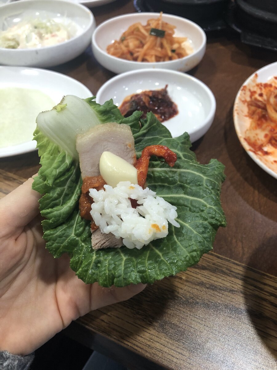 Блюдо под названием поссам - представляет собой вареную свинину, нарезанную кусочками. Есть ее нужно, как на фото, завернув в лист с соусом, кусочком кимчхи из дайкона, чесноком и рисом. Мы называем эту штуку "завернушка";)  Кроме мяса подают кучу закусок и два вида горячих супов. 
Такой ужин нам обходится в 14 тысяч вон (= 800 рублей) на двоих.    