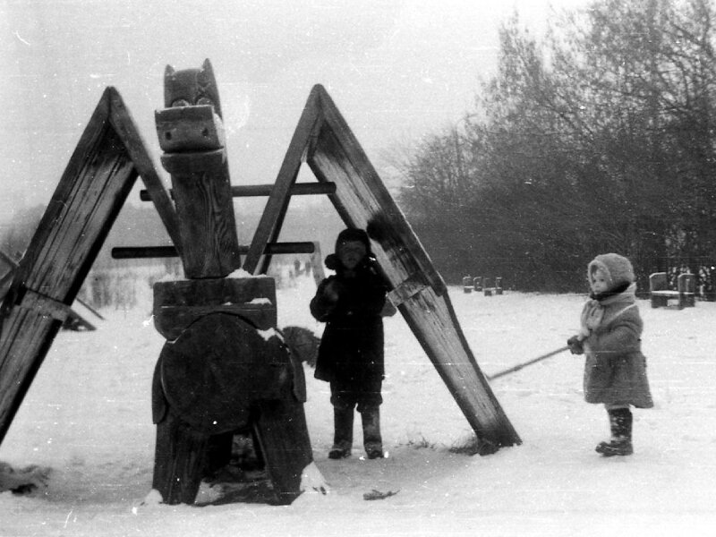 Фото сделано в период 1977-79 годов. Дети играют на площадке в юго-восточной части парка. Все игровые конструкции на ней были деревянными: грибочки, летучий змей (на фото), избушка, горка и т.д.